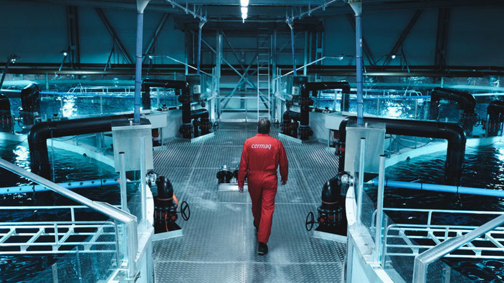 An employee walking between large tanks in a freshwater facility