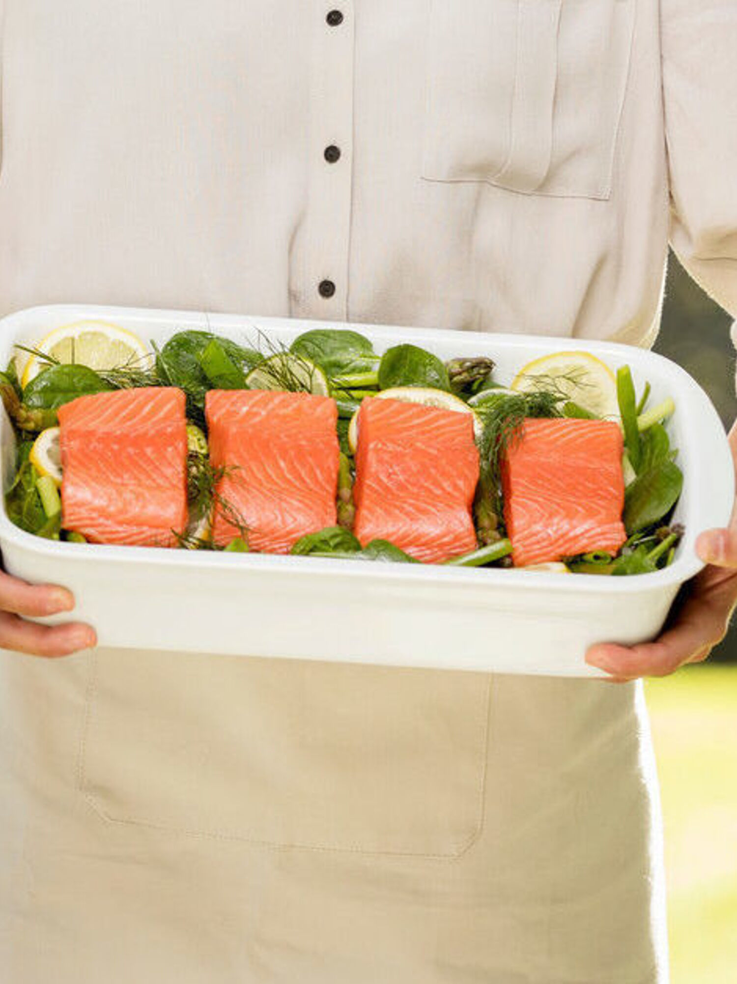 A person holds a serving dish with salmon pieces on vegetables